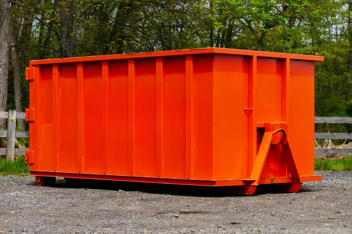 Orange roll-off dumpster on a gravel lot