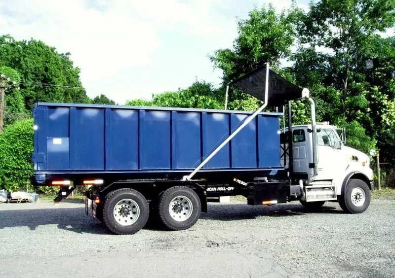 Roll-off truck carrying a dumpster with a tarp system